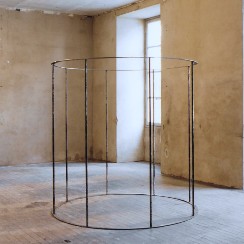 Une sculpture cylindrique en forme de cage, dont les barreaux sont assez espacés pour desssiner des portes.