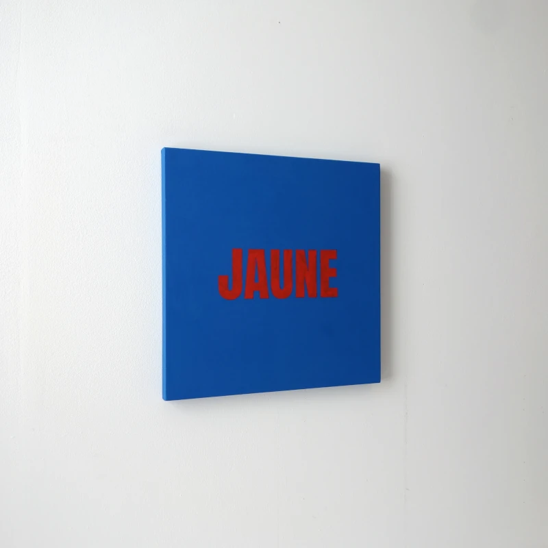Un tableau carré bleu avec le mot JAUNE écrit en rouge. Vue de trois-quarts.