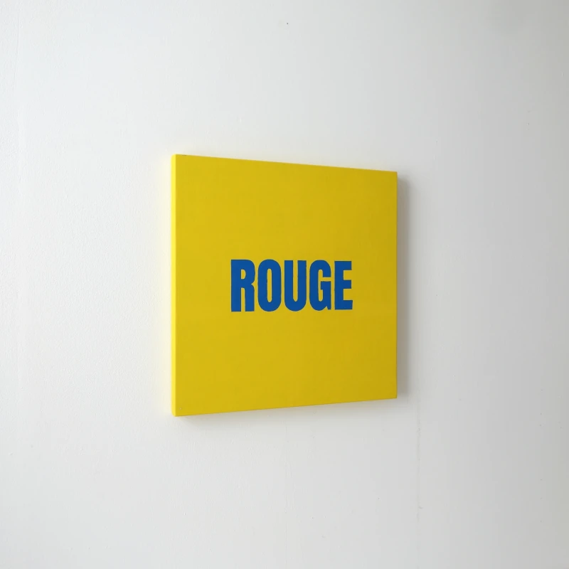 Un tableau carré jaune avec le mot ROUGE écrit en bleu. Vue de trois-quarts.