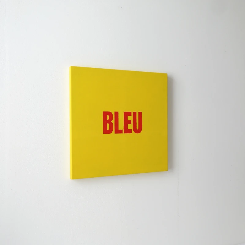 Un tableau carré jaune avec le mot BLEU écrit en rouge. Vue de trois-quarts.