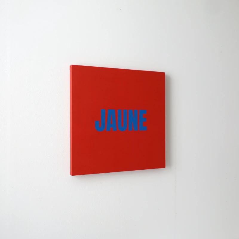 Un tableau carré rouge avec le mot JAUNE écrit en bleu. Vue de trois-quarts.