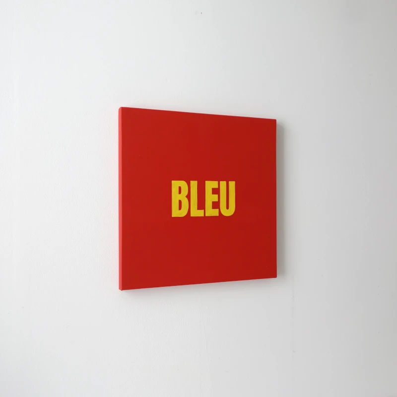 Un tableau carré rouge avec le mot BLEU écrit en jaune. Vue de trois-quarts.