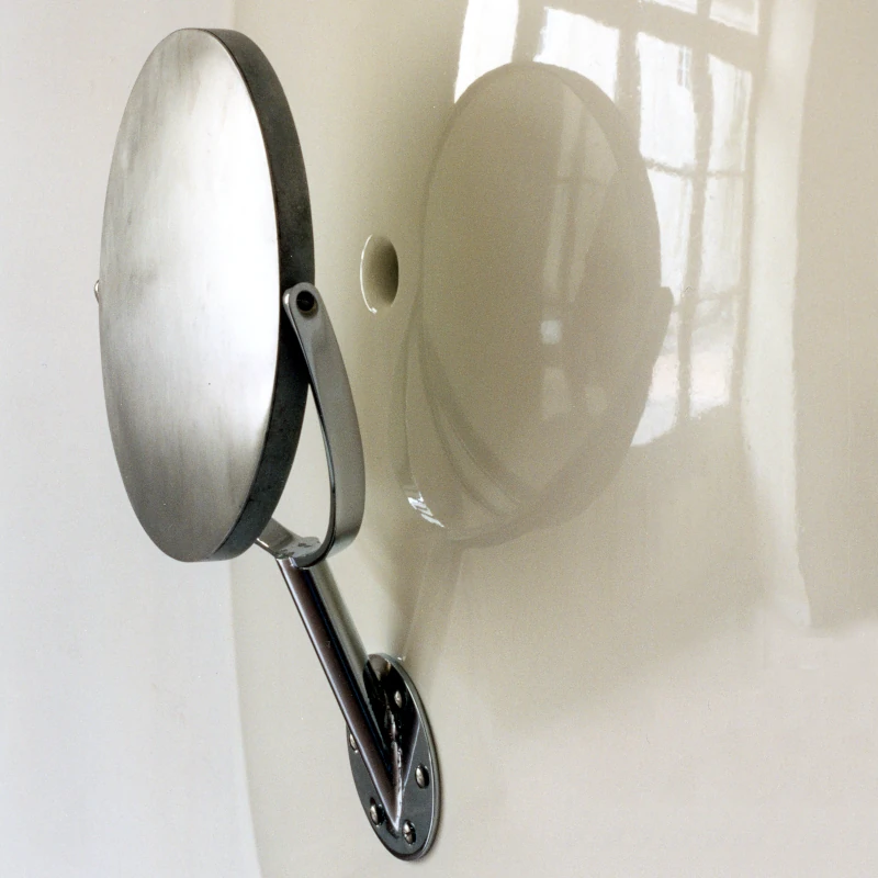 Un tableau mural vertical aux formes rondes, blanc brillant, cache son trou derrière un miroir rond.