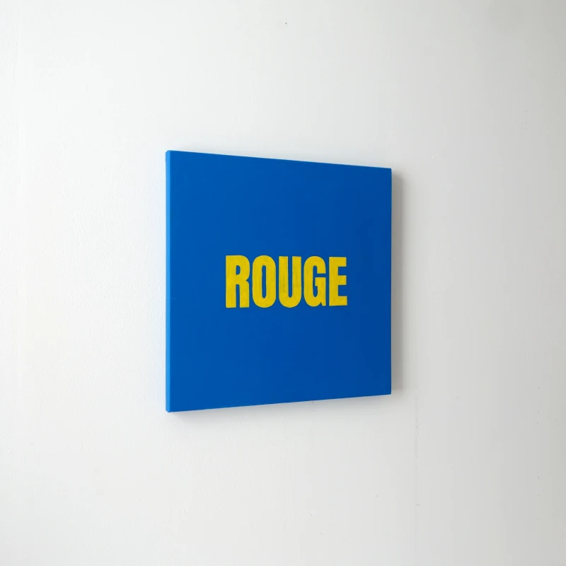 Un tableau carré bleu avec le mot ROUGE écrit en jaune. Vue de trois-quarts.